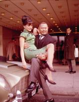 Harold Sakata in character as Oddjob from Goldfinger holds Hilton Hotel secretary Dawn Dunger in London 1965